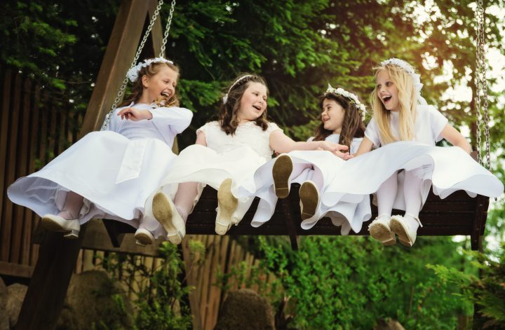cztery dziewczynki w komunijnych sukienkach na huśtawce, śmieją się